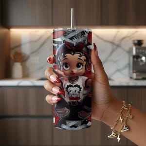 May include: A stainless steel tumbler with a Betty Boop design. The tumbler has a silver straw and a red, black, and white pattern. The Betty Boop graphic is wearing a white shirt and black pants. The tumbler is approximately 20 cm tall.