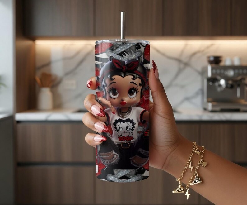 May include: A stainless steel tumbler with a Betty Boop design. The tumbler has a silver straw and a red, black, and white pattern. The Betty Boop graphic is wearing a white shirt and black pants. The tumbler is approximately 20 cm tall.