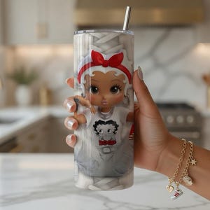 May include: A stainless steel tumbler with a cartoon character design, featuring a red bow and a white t-shirt with a graphic. The tumbler has a silver straw and a white and grey background.