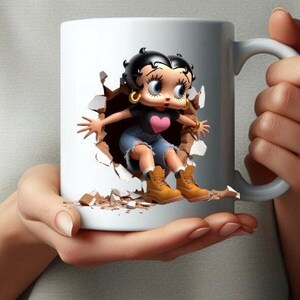 Puede incluir: Taza de cerámica blanca con una imagen de dibujos animados de una niña rompiendo la superficie de la taza. La niña lleva una camiseta negra, pantalones vaqueros azules y botas marrones. Tiene el pelo negro y un corazón rosa en la camiseta.