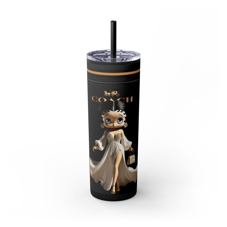 May include: Black tumbler with a black straw featuring a cartoon Betty Boop character in a white dress, holding a purse. The tumbler has the Coach logo and a gold band around the top.