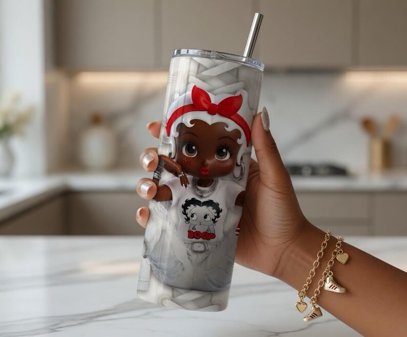 May include: A stainless steel tumbler with a cartoon character design. The character has a red bow and a white shirt. The tumbler has a silver straw and a clear lid. The background is grey and white.