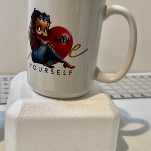 May include: White ceramic coffee mug with a cartoon image of Betty Boop sitting on a red heart that says "Jolly" and the text "Love Yourself".