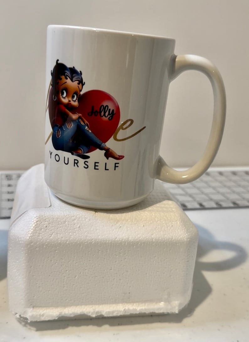May include: White ceramic coffee mug with a cartoon image of Betty Boop sitting on a red heart that says "Jolly" and the text "Love Yourself".