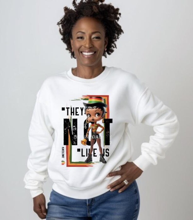 May include: White sweatshirt featuring a cartoon character with a hat and the text "THEY NOT LIKE US". The design includes a red, green, and yellow color scheme, with the word "Juneteenth" on the side.