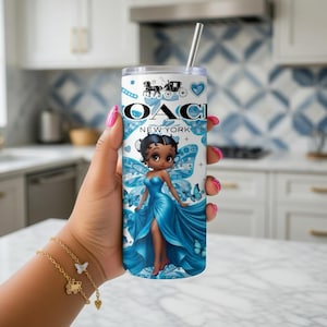 May include: A white and blue tumbler with a cartoon fairy design. The tumbler features the text "OACI NEW YORK" and a horse-drawn carriage logo. The fairy is wearing a blue dress and has blue butterfly wings. A silver straw is inserted in the tumbler.