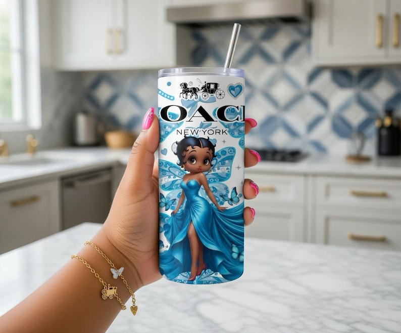 May include: A white and blue tumbler with a cartoon fairy design. The tumbler features the text "OACI NEW YORK" and a horse-drawn carriage logo. The fairy is wearing a blue dress and has blue butterfly wings. A silver straw is inserted in the tumbler.