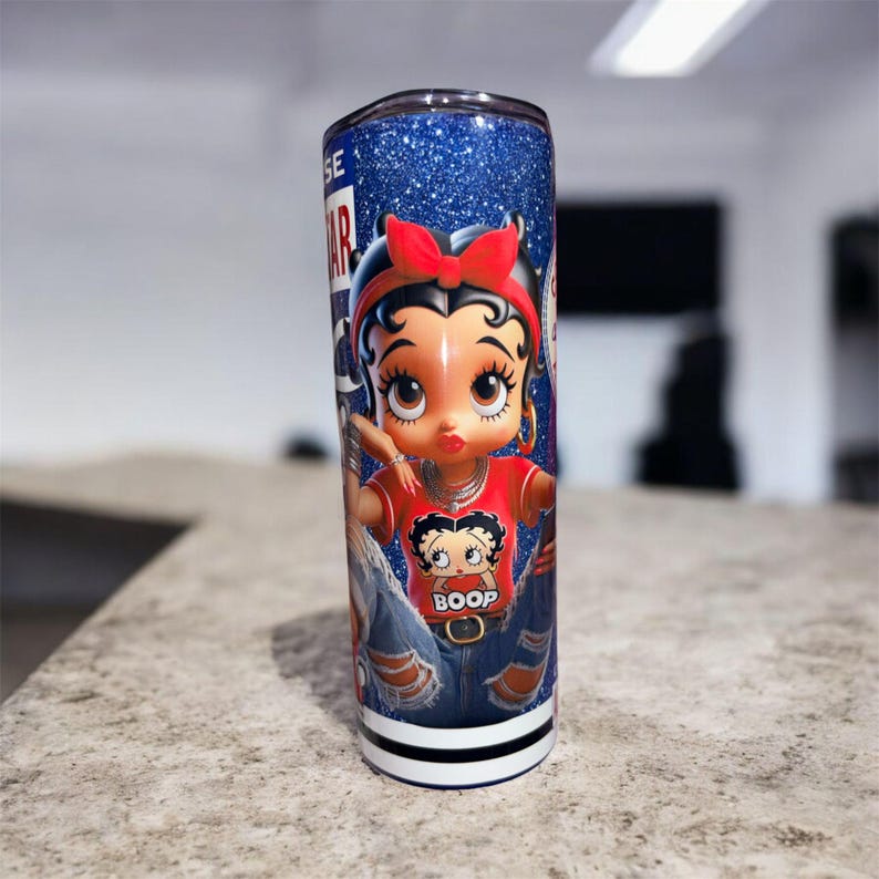 May include: A stainless steel tumbler with a glittery blue background and a cartoon image of Betty Boop. Betty Boop is wearing a red shirt with the word "Boop" and blue jeans. The tumbler has a black and white stripe at the bottom.