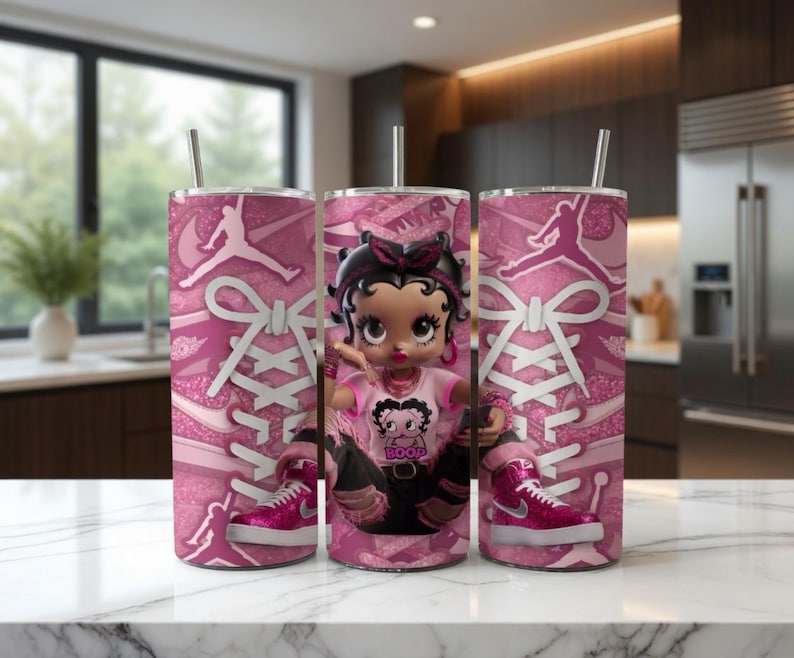 May include: Pink tumbler with a Betty Boop doll and a pink and white sneaker design. The tumbler features a silver straw and a pink and white shoelace design. The Betty Boop doll is wearing a pink shirt and black pants.