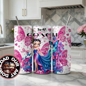 May include: Three white tumblers with pink butterfly and heart designs. One tumbler features a Betty Boop illustration and the Coach New York logo. Each tumbler has a silver straw. The tumblers are on a white countertop.
