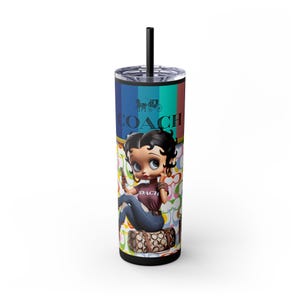 May include: A tall, black and silver tumbler with a black straw. The tumbler features a colorful design with the word "COACH" and a cartoon image of Betty Boop. The tumbler is decorated with a Coach logo and a pattern.