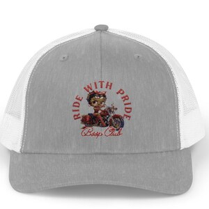 May include: A gray and white trucker hat with a red, white, and blue embroidered design. The design features a cartoon character riding a motorcycle with the text "Ride With Pride Boop Club".