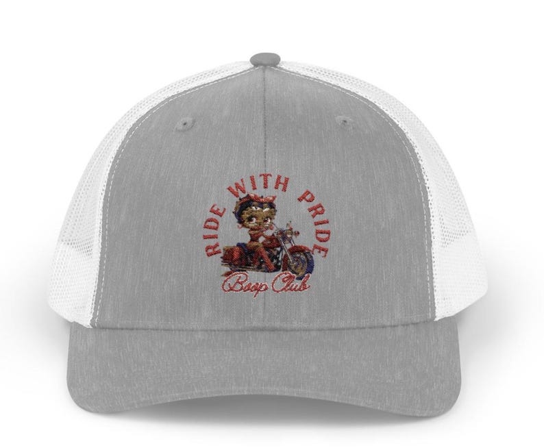 May include: A gray and white trucker hat with a red, white, and blue embroidered design. The design features a cartoon character riding a motorcycle with the text "Ride With Pride Boop Club".