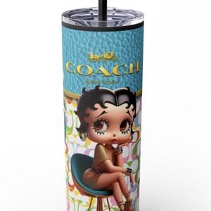May include: A blue and white tumbler with a black lid and straw. The tumbler features a cartoon image of a woman sitting on a chair with the text "COACH NEW YORK" above her. The background is a pattern of colorful "C" shapes.