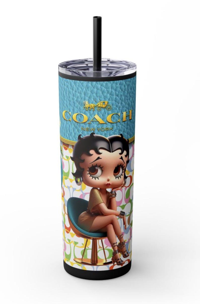 May include: A blue and white tumbler with a black lid and straw. The tumbler features a cartoon image of a woman sitting on a chair with the text "COACH NEW YORK" above her. The background is a pattern of colorful "C" shapes.