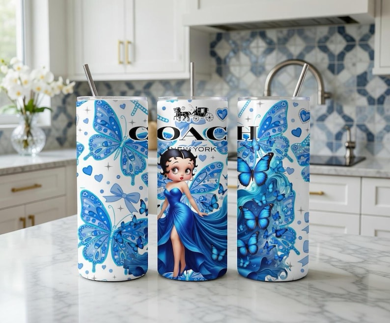 Może przedstawiać: Trzy białe kubki ze stali nierdzewnej z niebieskimi wzorami motyli i serc. Jeden kubek ma grafikę Betty Boop i logo Coach New York. Każdy kubek ma srebrną słomkę i pokrywkę.