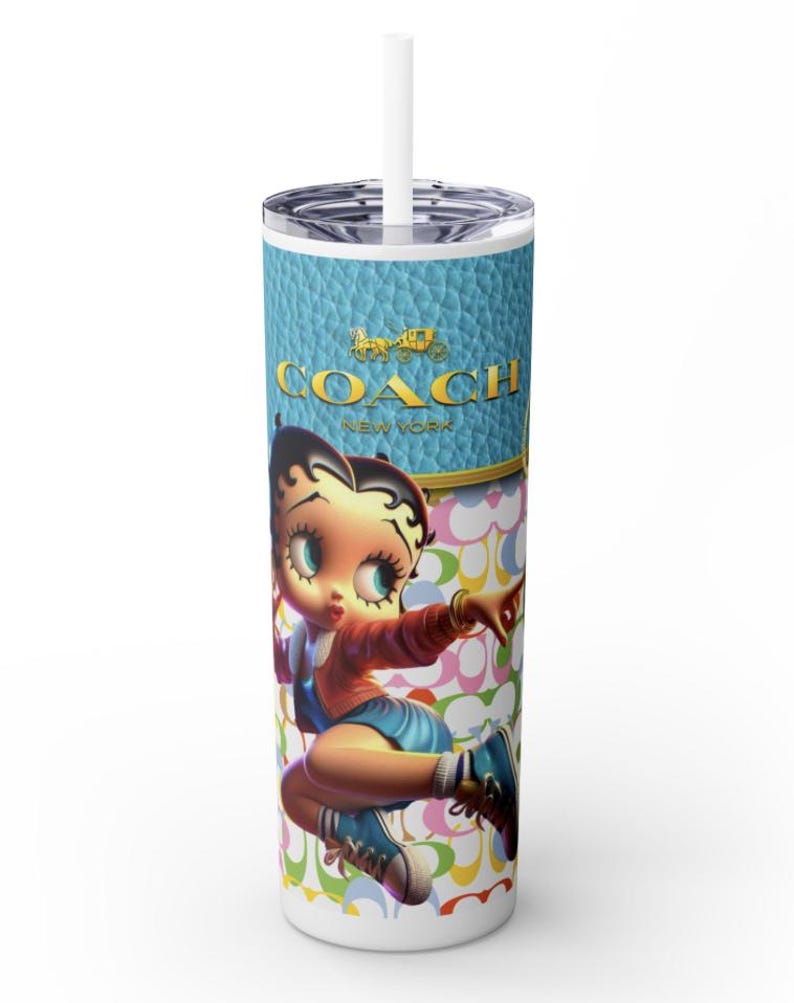 May include: A tall, white tumbler with a lid and straw. The tumbler features a cartoon image of Betty Boop in a red jacket and blue shorts. The top section has a blue leather-like texture with the gold "COACH NEW YORK" logo. The background has a repeating pattern.