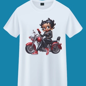 May include: White t-shirt with a cartoon image of a woman riding a red motorcycle. The woman is wearing a black leather jacket, black pants, and red shoes. She is holding a red phone in her hand.