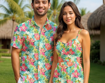 May include: A man and a woman are wearing matching tropical floral print outfits. The man is wearing a short-sleeved button-down shirt and white shorts. The woman is wearing a sundress with spaghetti straps. The print features pink, orange, and green flowers.