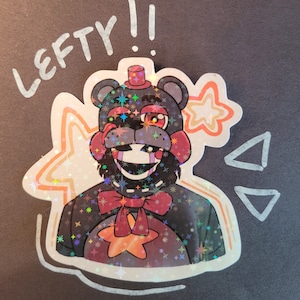 May include: A sticker featuring a cartoon character with a red bow tie and a red hat. The character has a black and red colour scheme and is surrounded by a holographic background with stars. The sticker says "Lefty!" in white text.