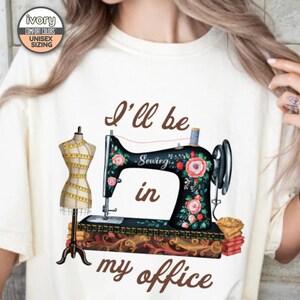 May include: A white t-shirt with the text "I'll be in my office" and a vintage sewing machine with floral accents. The sewing machine is on a table with a fabric dummy next to it.
