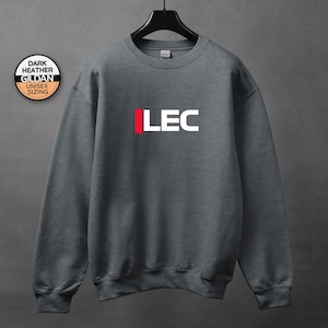 May include: Dark heather gray Gildan unisex sweatshirt with the letters "LEC" in white with a red vertical bar. The sweatshirt is hanging on a black hanger against a gray background. A round sticker with text is in the upper left corner.