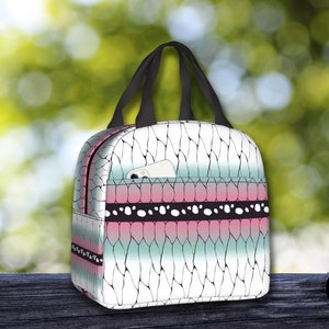 K&ouml;nnte beinhalten: Eine wei&szlig;e Lunch-Tasche mit einem geometrischen Muster in Schwarz und Rosa. Die Tasche hat einen schwarzen Griff und eine kleine Tasche auf der Vorderseite.