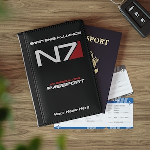 May include: A black passport holder with the text "SYSTEMS ALLIANCE N7" and "N7 SPECIAL OPS PASSPORT" in white. The holder has a red N7 logo and the text "Your Name Here" in white.