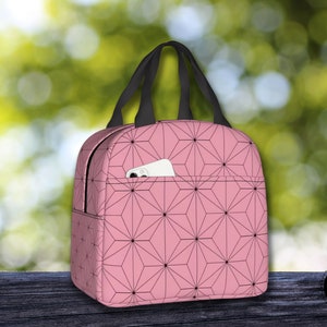 K&ouml;nnte beinhalten: Rosa Lunch Bag mit einem schwarzen geometrischen Muster und einer kleinen Tasche auf der Vorderseite. Die Tasche hat einen schwarzen Griff.