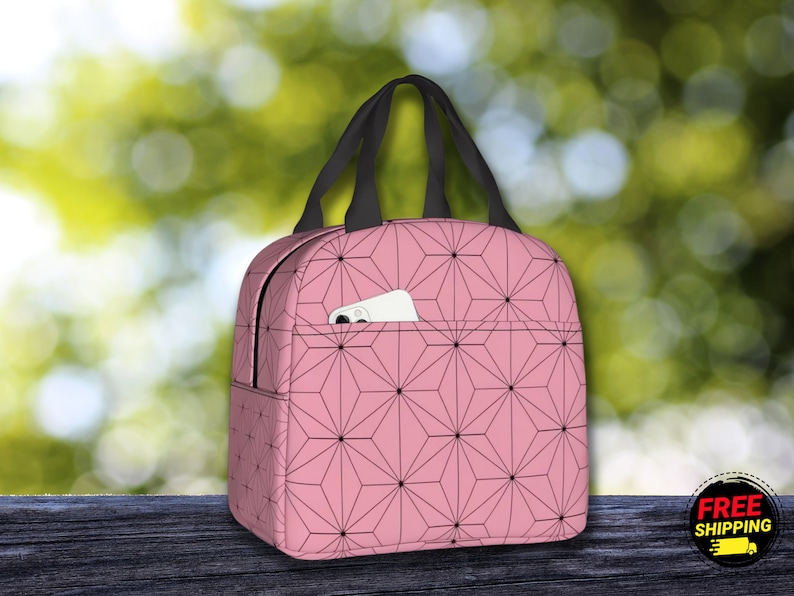 K&ouml;nnte beinhalten: Rosa Lunch Bag mit einem schwarzen geometrischen Muster und einer kleinen Tasche auf der Vorderseite. Die Tasche hat einen schwarzen Griff.