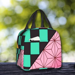 K&ouml;nnte beinhalten: Eine schwarz-gr&uuml;ne karierte Lunch-Tasche mit einem pink-wei&szlig;en geometrischen Muster an der Seite. Die Tasche hat einen schwarzen Griff und eine kleine Tasche auf der Vorderseite.