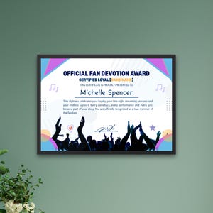 May include: Framed certificate with the text "OFFICIAL FAN DEVOTION AWARD" and "Michelle Spencer". The certificate has a colorful design with musical notes and a crowd silhouette. The frame is black.