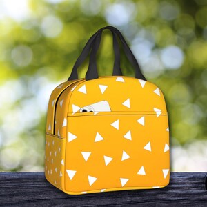 K&ouml;nnte beinhalten: Gelbe Lunchtasche mit einem wei&szlig;en Dreiecksmuster. Die Tasche hat einen schwarzen Griff und eine kleine Tasche auf der Vorderseite.