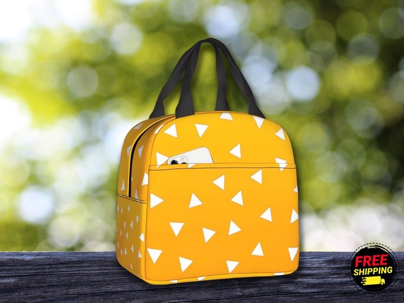 K&ouml;nnte beinhalten: Gelbe Lunchtasche mit einem wei&szlig;en Dreiecksmuster. Die Tasche hat einen schwarzen Griff und eine kleine Tasche auf der Vorderseite.