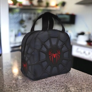 May include: Black lunch bag with a red spider web design and a red spider logo.