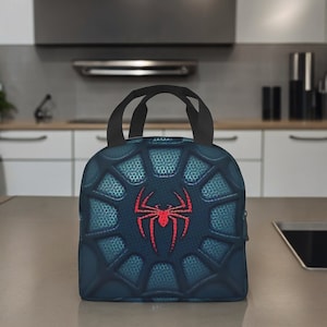 May include: A blue lunch bag with a black zipper and two black handles. The bag features a spider web design with a red spider in the centre.