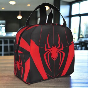 May include: Black and red lunch bag with a spider web design. The spider web is red and the spider is red with a black body.