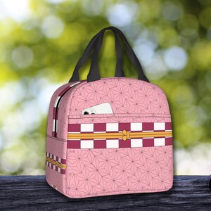 K&ouml;nnte beinhalten: Rosa Lunch Bag mit kariertem Muster und Blumendesign. Die Tasche hat einen Rei&szlig;verschluss und einen oberen Griff.