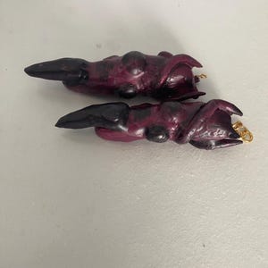 May include: Two purple and black dragon claws with gold rings attached. The claws are made of polymer clay and have a textured surface.
