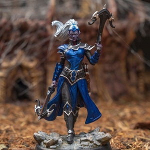 May include: A blue and black painted miniature figurine of a female elf warrior with white hair, holding a crossbow. The figurine is standing on a rocky base.