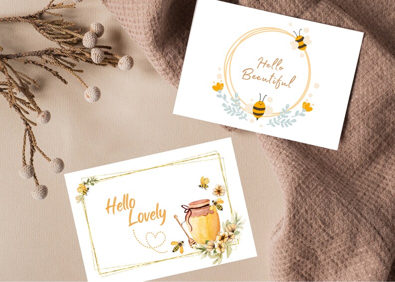 Puede incluir: Dos tarjetas de felicitaci&oacute;n con marcos dorados y dise&ntilde;os con tem&aacute;tica de abejas. La primera tarjeta dice "Hello Beautiful" con una abeja y flores. La segunda tarjeta dice "Hello Lovely" con una abeja, un tarro de miel y flores.