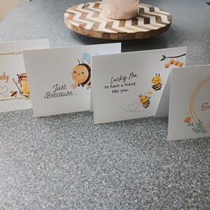 Puede incluir: Cuatro tarjetas de felicitaci&oacute;n con ilustraciones de abejas y texto. Las tarjetas dicen "Hello Lovely", "Just Because", "Lucky Me to have a friend like you", y "Hello Beautiful".