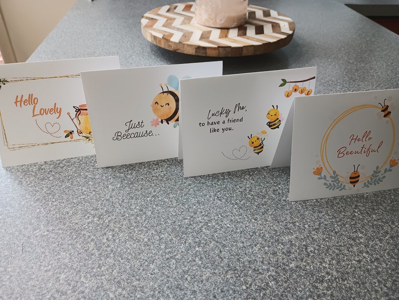 Puede incluir: Cuatro tarjetas de felicitaci&oacute;n con ilustraciones de abejas y texto. Las tarjetas dicen "Hello Lovely", "Just Because", "Lucky Me to have a friend like you", y "Hello Beautiful".