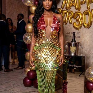 Può includere: Una donna con un abito di paillettes a una festa di compleanno. L'abito passa dal rosso all'oro e al verde, con un design a rete in vita. Palloncini dorati e bordeaux e uno striscione di palloncini "Happy 30th" sullo sfondo.