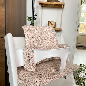 Op de afbeelding: Een witte kinderstoel met een zitkussen en rugleuning met een roze en witte dierenprint. De stoel heeft een witte veiligheidsbeugel en is ontworpen voor een baby of peuter.