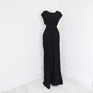 Puede incluir: Un vestido negro largo con un corpiño ajustado y una falda fluida. El vestido presenta un diseño sencillo y elegante con cuello redondo y mangas cortas. Un cinturón a juego ciñe la cintura. El vestido se exhibe en un maniquí de alambre sobre un fondo blanco.