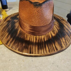 May include: A wide-brimmed straw hat with a brown ribbon band. The hat is sitting on a wooden base with a dark brown finish.