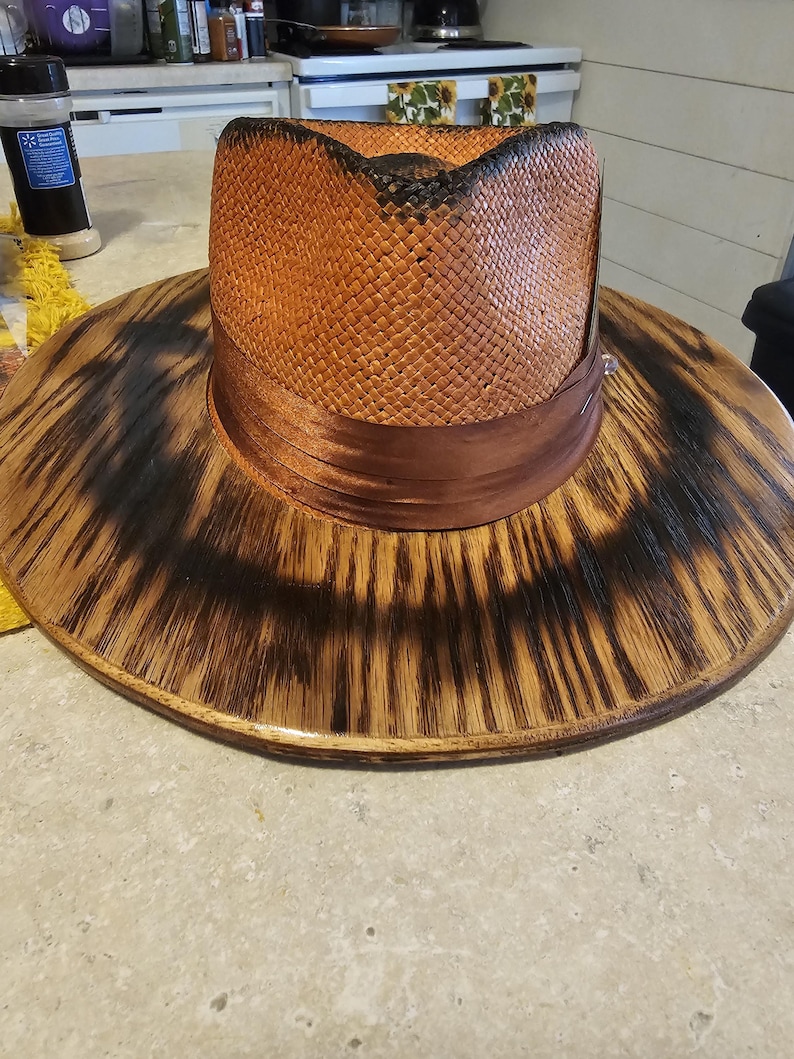 May include: A wide-brimmed straw hat with a brown ribbon band. The hat is sitting on a wooden base with a dark brown finish.