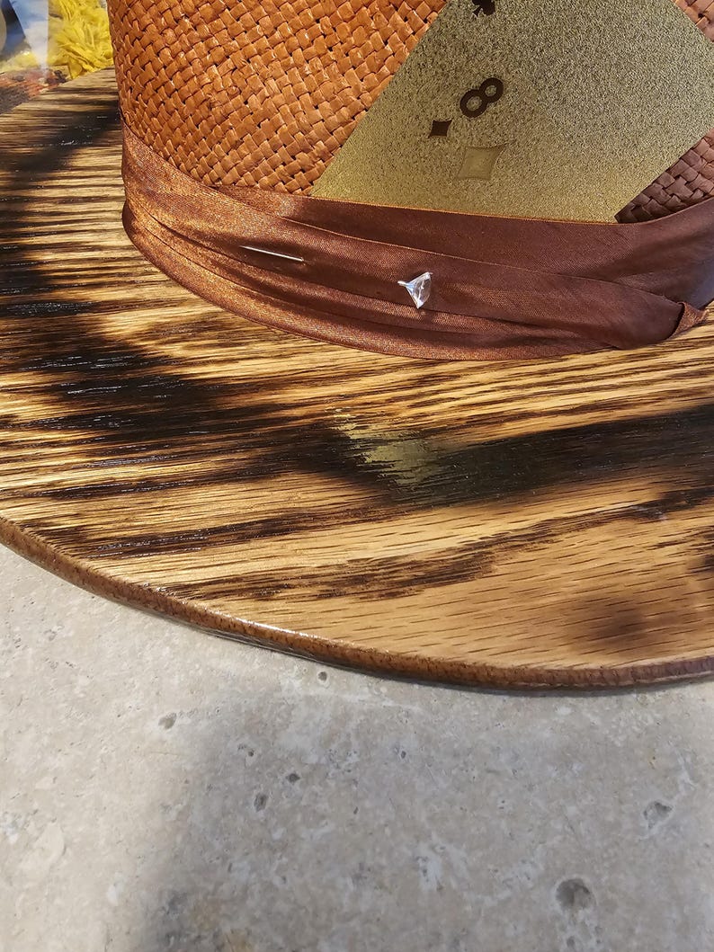 May include: A brown woven hat with a brown ribbon and a gold patch with the number "8" on it. The hat is sitting on a wooden base.