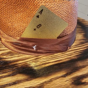 May include: A brown woven straw hat with a brown ribbon and a gold playing card with the number 4 of clubs on it.